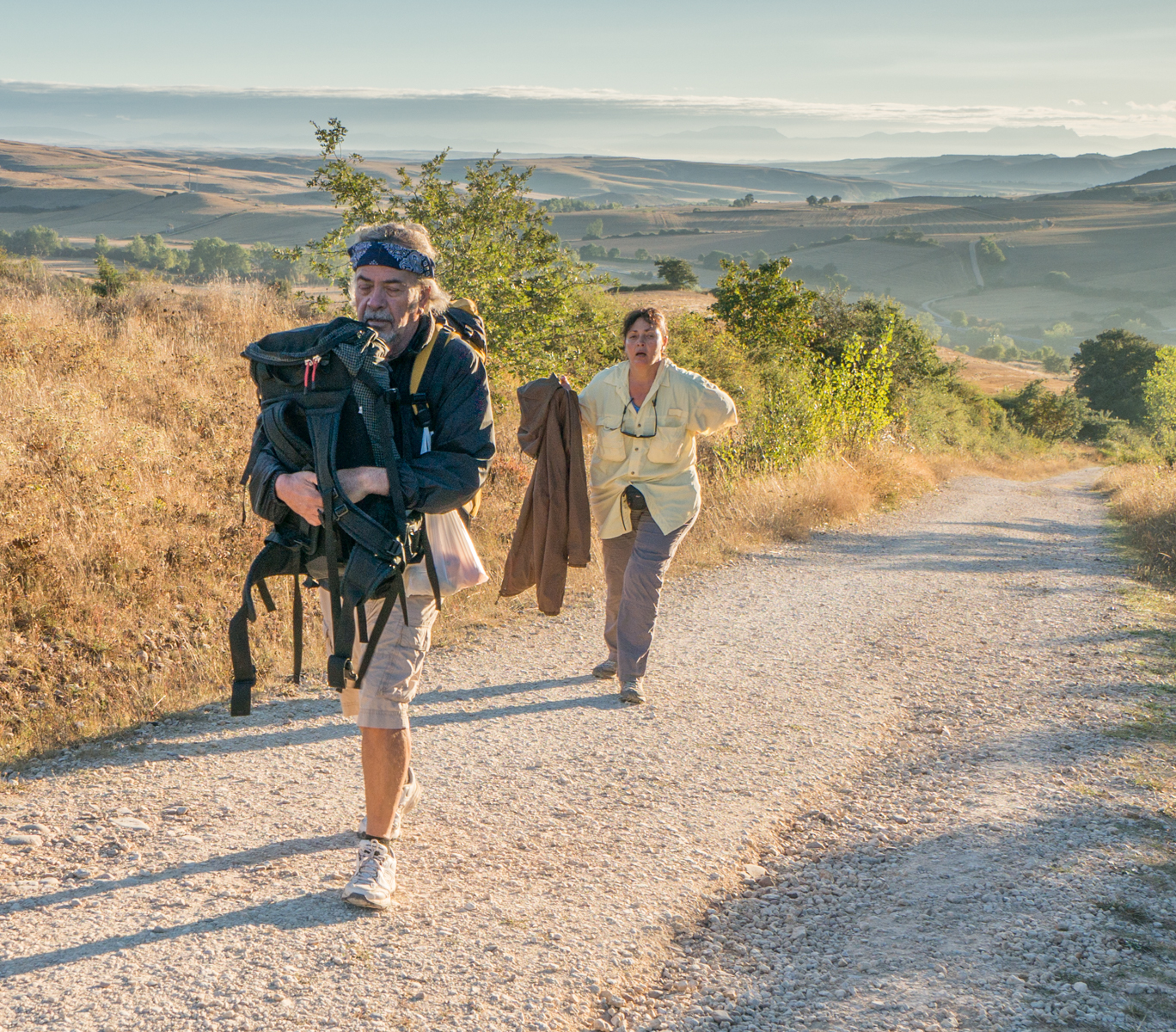 A pilgrim on the Camino Frances carries his wife's backpack up a hill | Photo by Mike Hudak