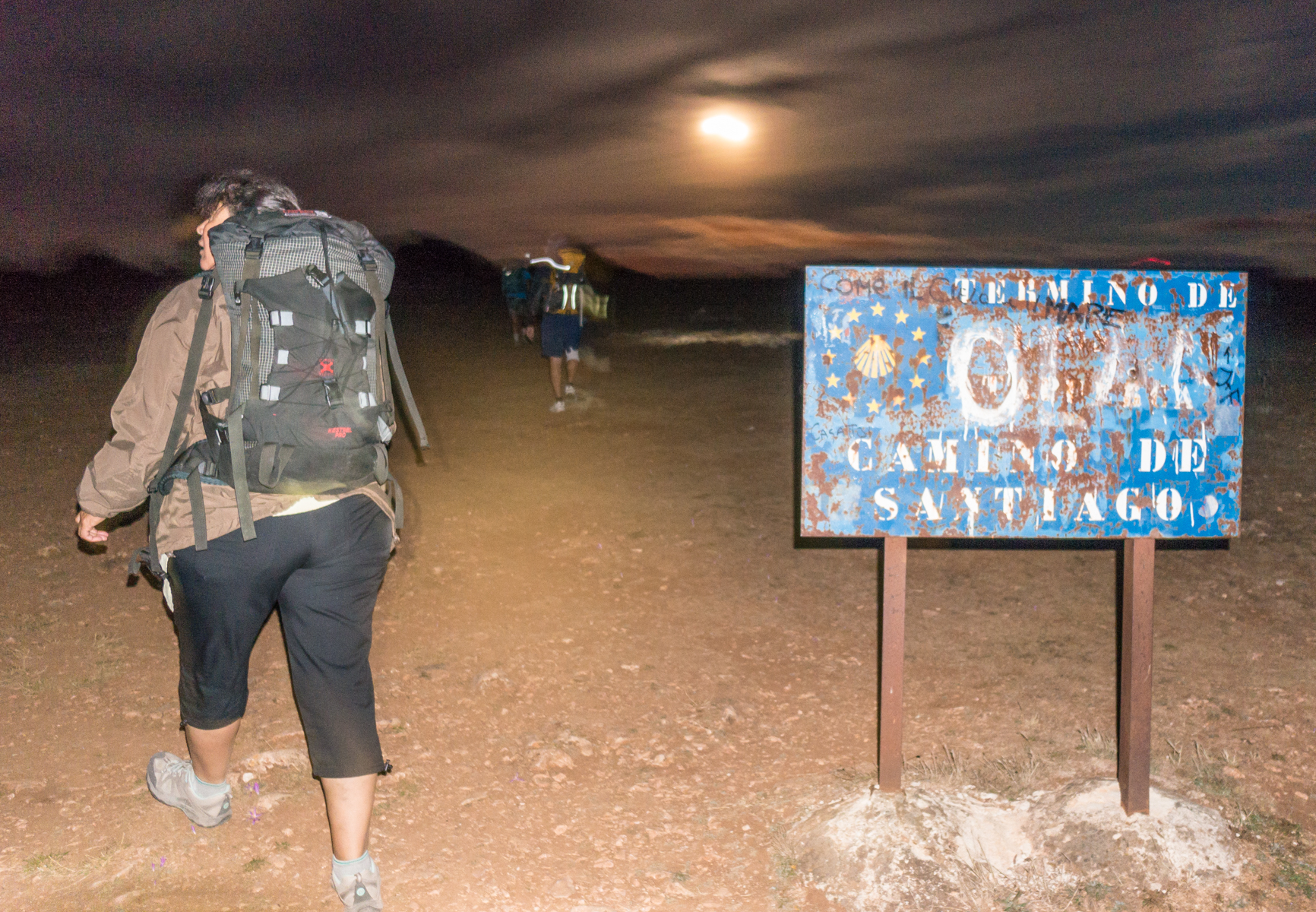 Pilgrims pass a marker for a deceased pilgrim on the Camino Frances 2.4 km west of Atapuerca, Spain | Photo by Mike Hudak