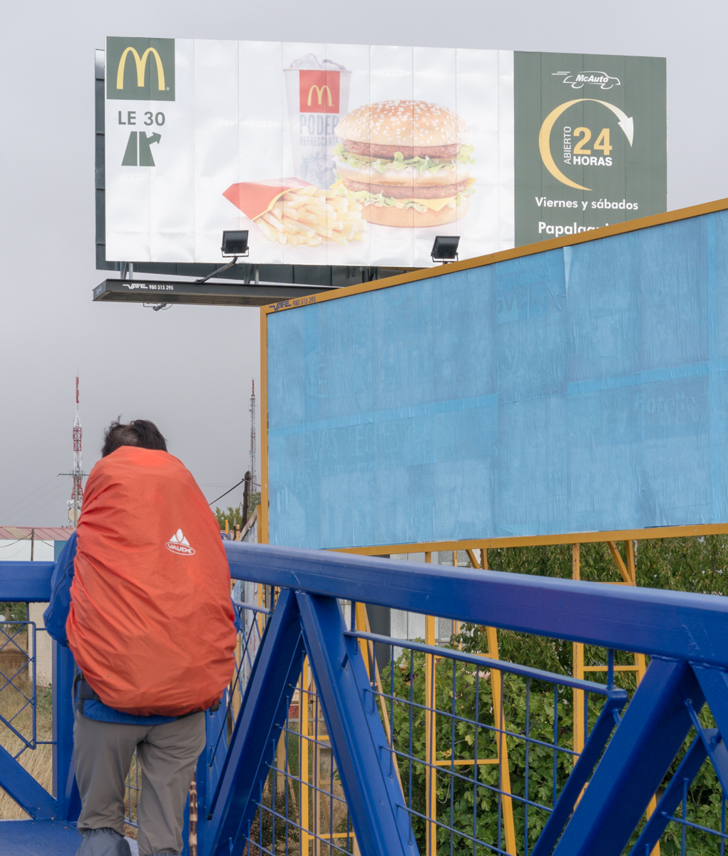 A pilgrim confronts a McDonald's billboard on the Camino Frances in Valdelafuente, an eastern suburb of Leon, Spain | Photo by Mike Hudak